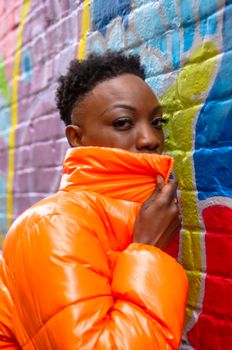 A striking portrait of a woman in an orange jacket against a colorful graffiti wall.