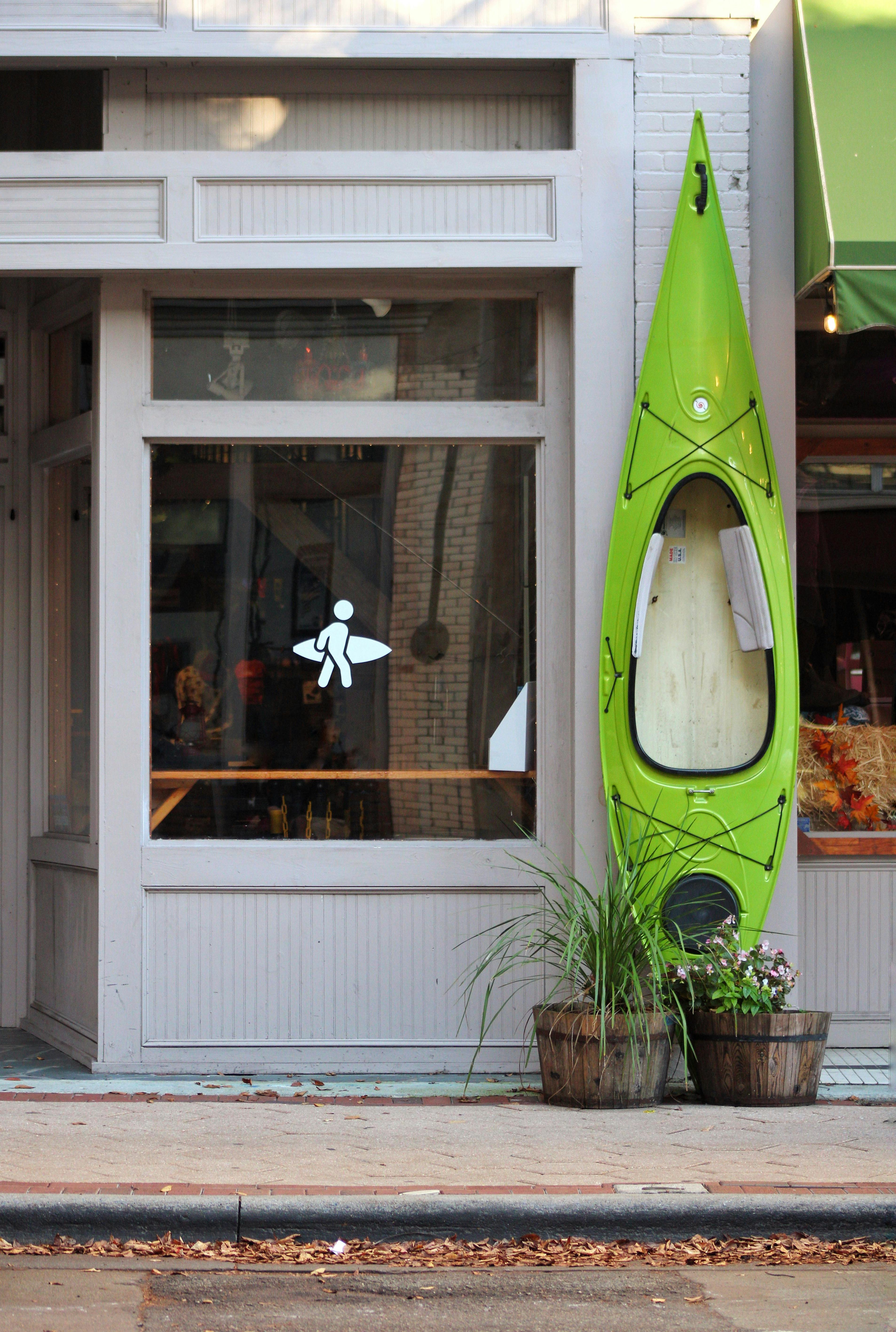 Outdoor store storefront featuring a vertical green kayak against a charming facade.