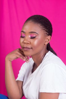 Close-up portrait of a woman with braided hair and vibrant pink makeup against a matching background.