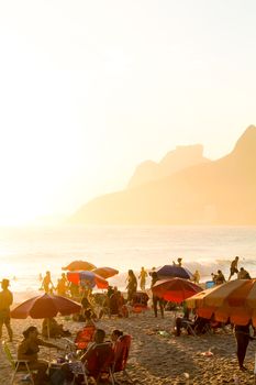 A bustling beach scene at sunset with colorful umbrellas and people enjoying the shore.