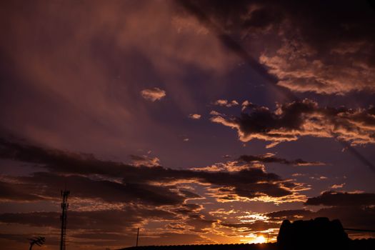 Capture of a dramatic sunset sky filled with orange clouds and silhouetted structures, creating a moody atmosphere.
