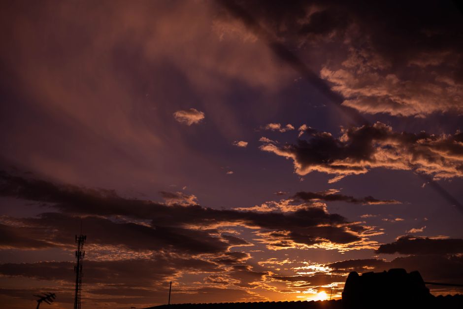 Capture of a dramatic sunset sky filled with orange clouds and silhouetted structures, creating a moody atmosphere.
