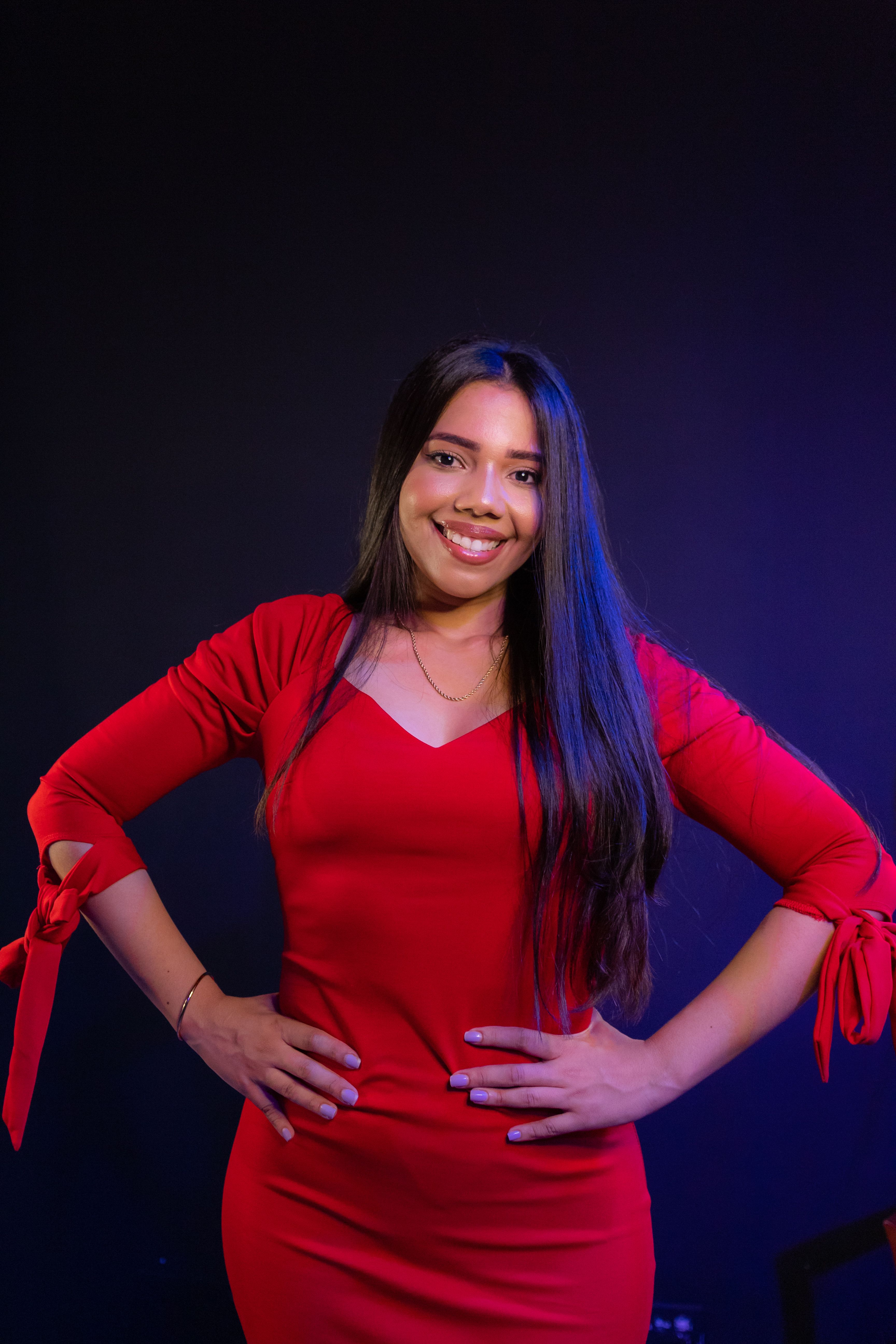 Studio portrait of a smiling woman in a red dress against a dark background.