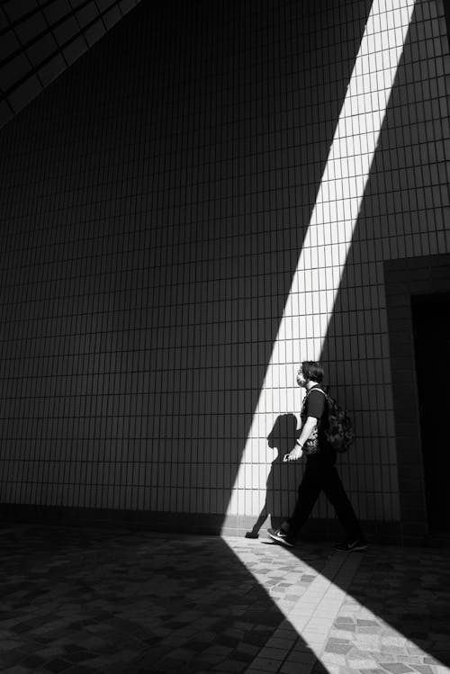 Free Grayscale Photo of a Person Walking while Carrying a Bag Stock Photo