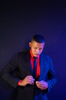 Portrait of a man adjusting his suit button against a purple background in a formal attire.