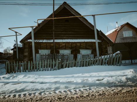 A rustic wooden house with a snow-covered fence in a winter setting, showcasing vintage charm.