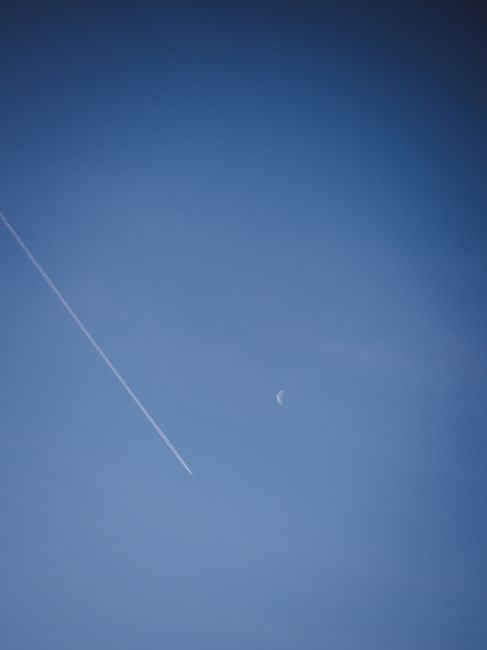 Crescent moon with contrail streak against a clear blue sky, capturing serene atmosphere.
