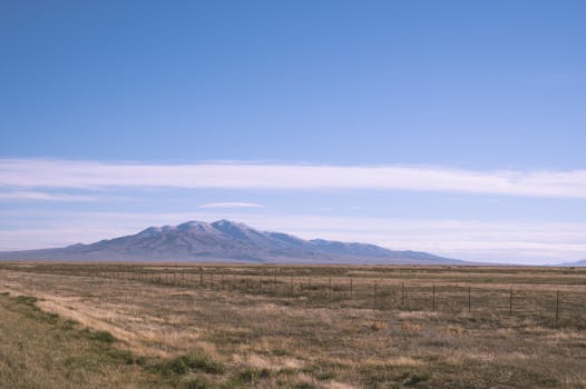 A wide open field with mountain under a clear blue sky, capturing the serenity of nature.