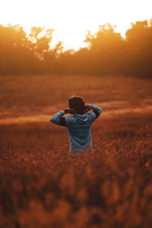 A Person Standing on a Grass Field during Sunset