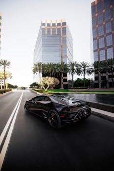 High-end black sports car driving through a modern urban area with palm trees and skyscrapers.