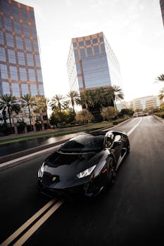 A luxurious black sports car driving on a modern urban road with skyscrapers in the background.