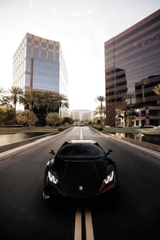 Black Lamborghini driving on a city street flanked by modern skyscrapers.