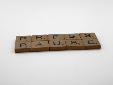 Wooden Scrabble tiles arranged to spell 'Press Pause' on a clean white background.