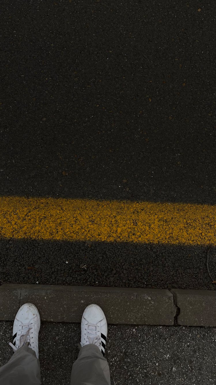 Person Wearing White Sneakers Standing On A Gutter 