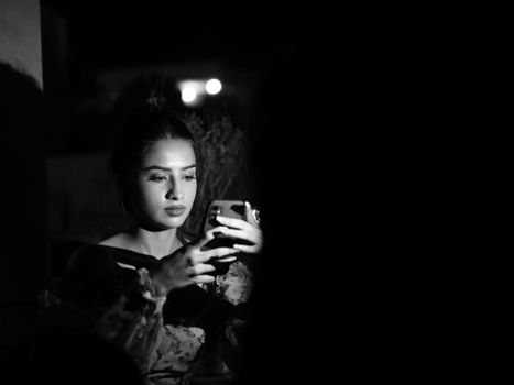 A woman focused on her smartphone in a dramatic black and white setting.