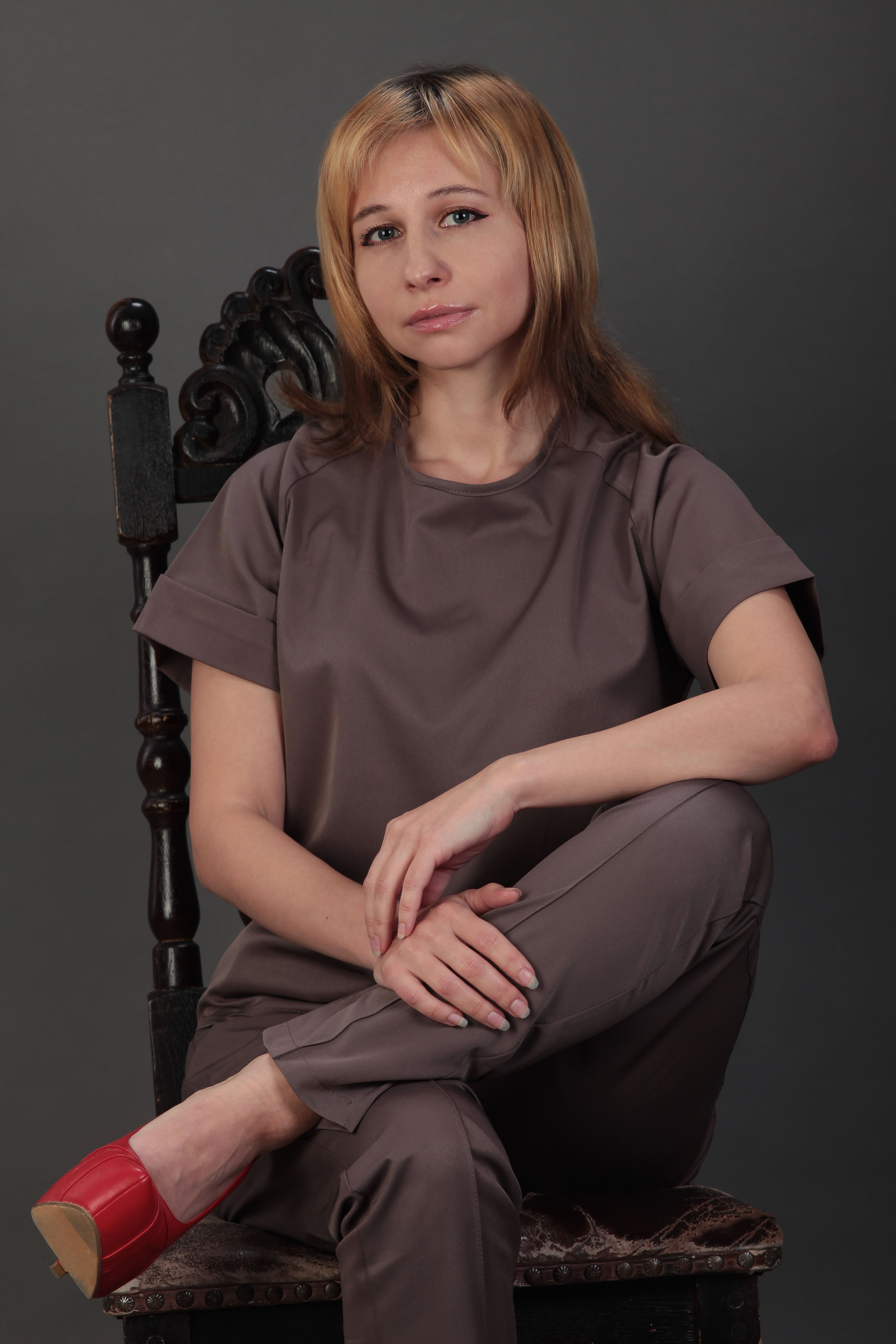 Portrait of a stylish woman seated on a vintage chair with a neutral background, showcasing elegance.