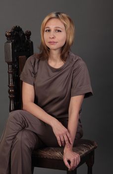 Elegant headshot of a woman sitting on a wooden chair with gray background.
