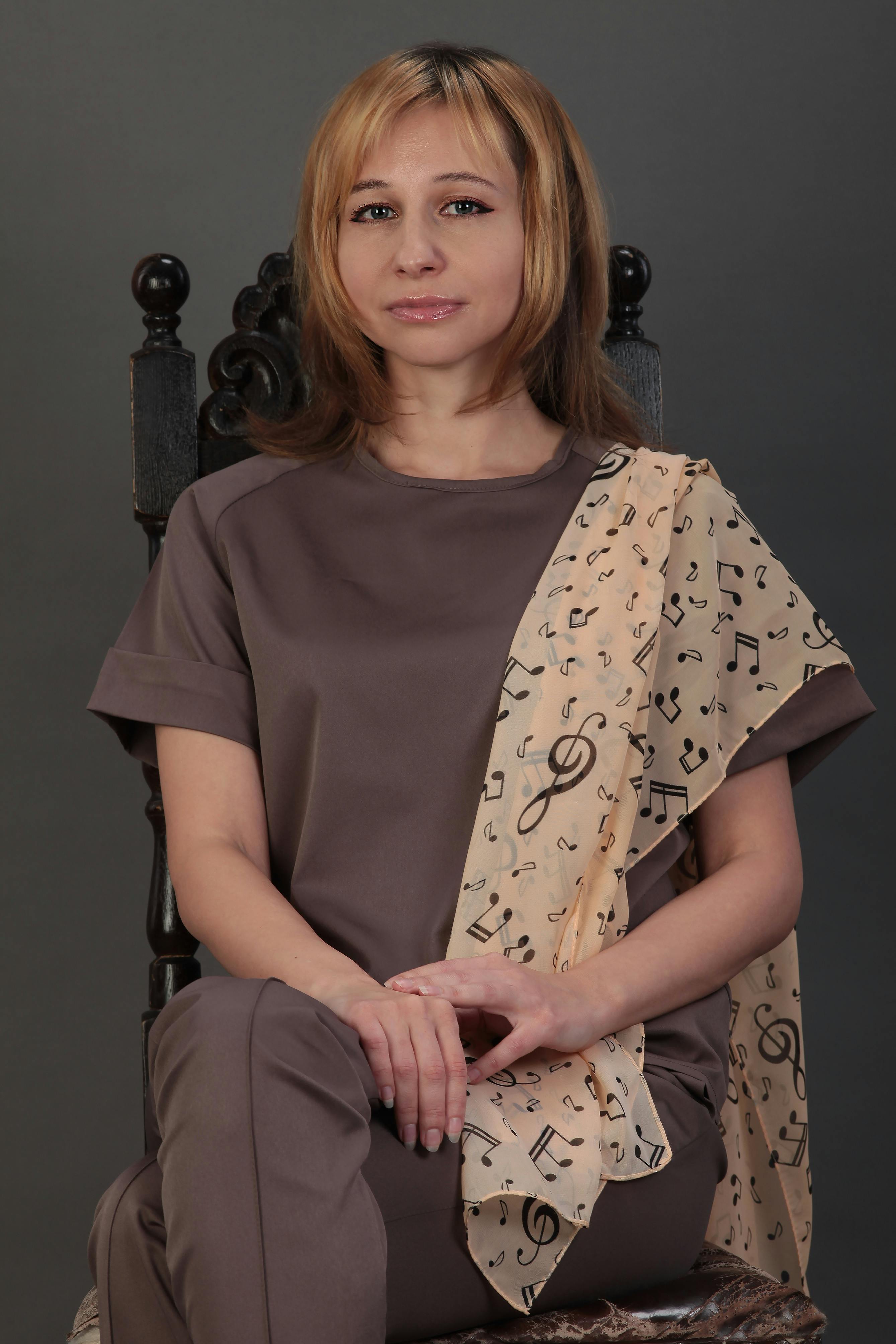 Elegant portrait of a woman sitting in a studio, wearing a musical note scarf, exuding fashion and beauty.
