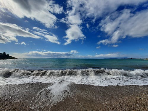 Ocean Waves Crashing on Shore Under Blue Sky and White Clouds