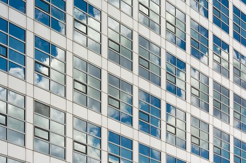 Free A modern glass building facade reflecting a clear blue sky with clouds. Captured from a low angle for dramatic effect. Stock Photo