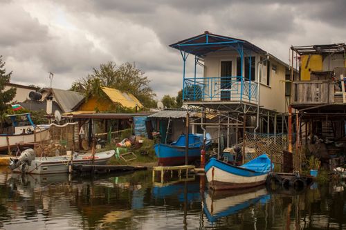 Free Charming rural Bulgarian village with boats docked along the river, showcasing rustic architecture. Stock Photo