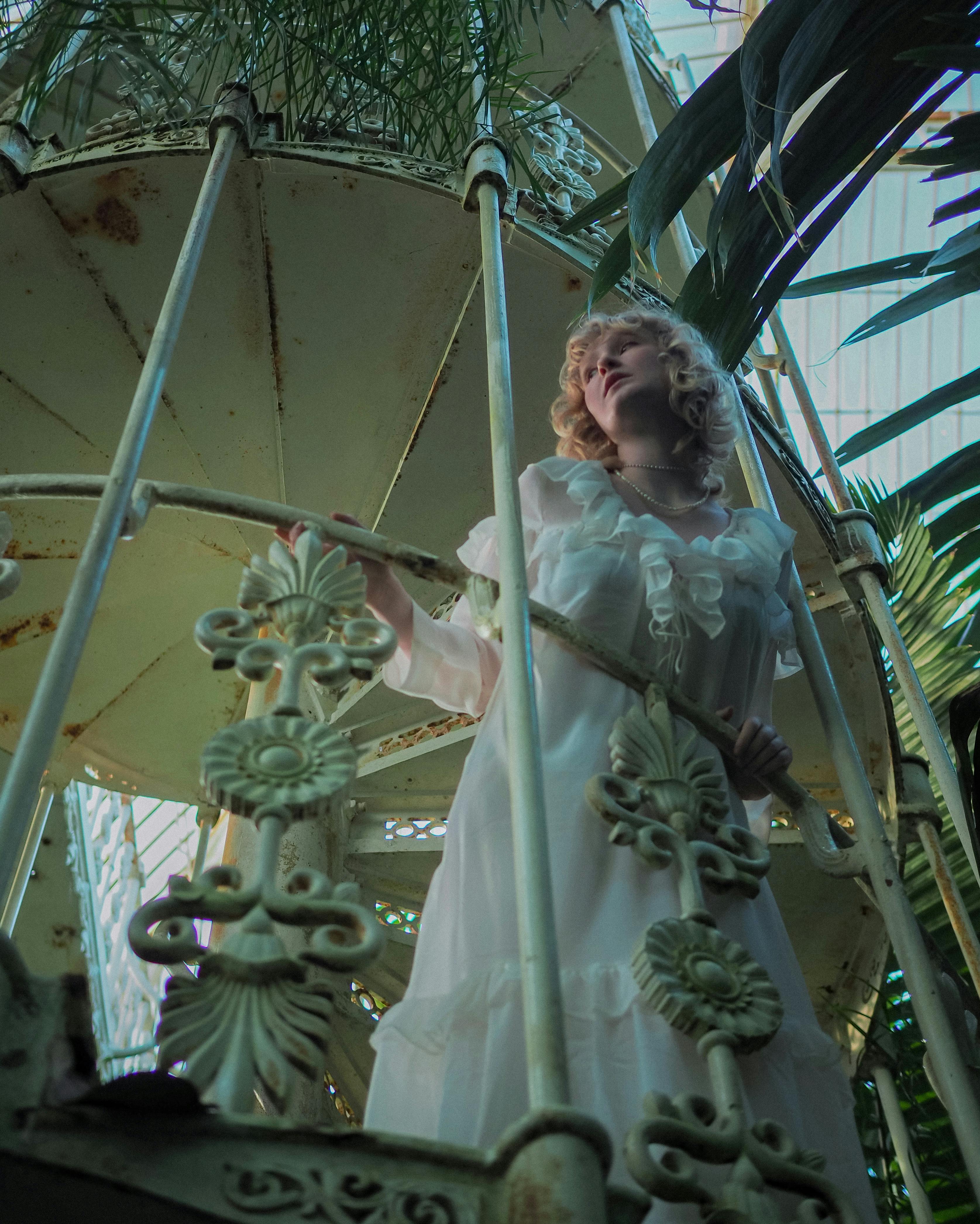 Victorian woman gracefully posing on an ornate spiral staircase surrounded by plants.