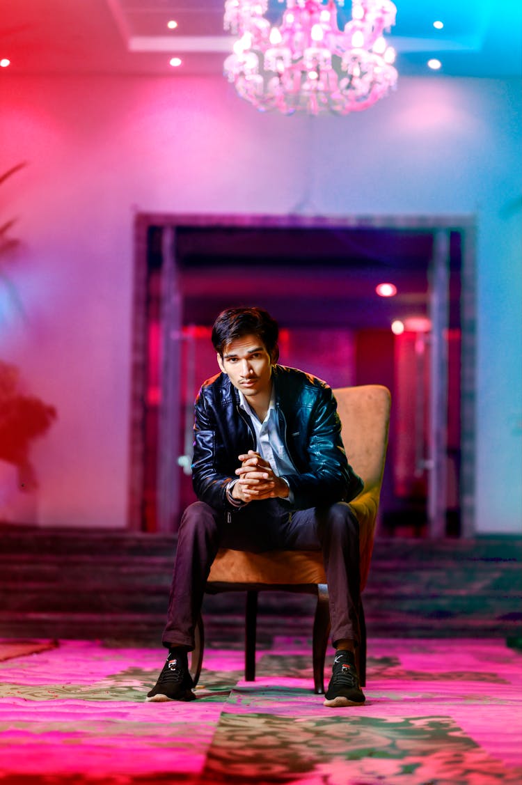 A Man In A Leather Jacket Sitting On A Chair