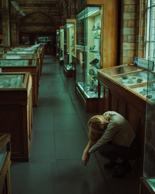 Free A weary woman leans in a quiet museum corridor, capturing exhaustion and solitude. Stock Photo