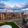 An aerial view of a sprawling oil refinery complex bathed in warm sunset light under a cloudy sky.