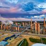 An aerial view of a sprawling oil refinery illuminated under a colorful evening sky.