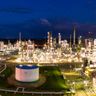 Aerial view of a sprawling oil refinery glowing brightly with complex lights against a dark night sky.