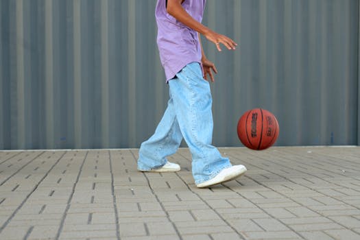 Casual street style photo of a person dribbling a basketball on a paved outdoor area.