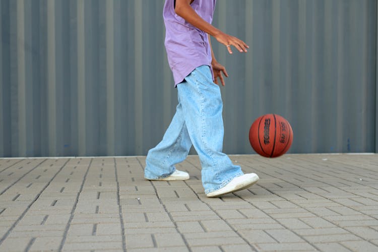 A Person Wearing Denim Pants Near A Bouncing Basketball Ball