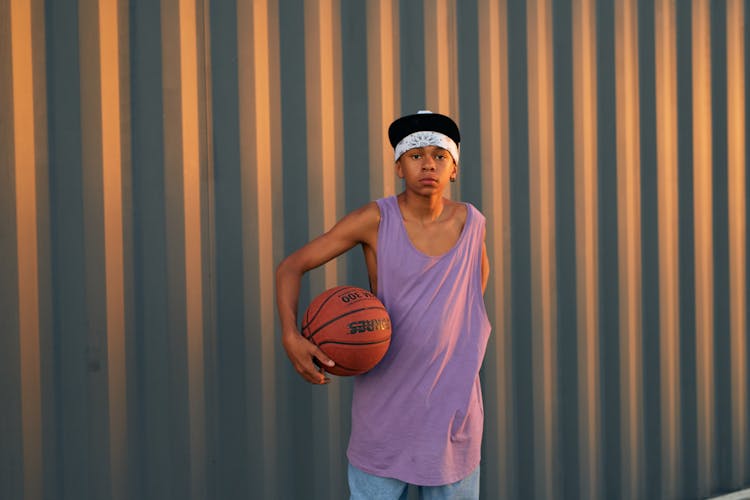 A Boy Wearing A Bandana And A Cap Holding A Ball