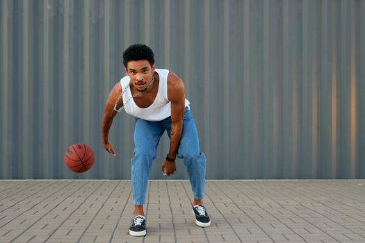 A stylish young man dribbles a basketball, showcasing sporty fashion outdoors.