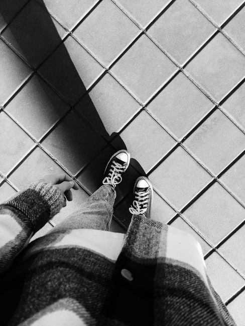 Top-down view of a person in sneakers standing on a tiled floor, casting a shadow.