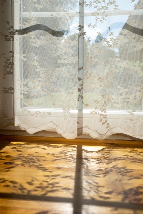 Free Sunlight casts intricate shadows through elegant lace curtains on a wooden floor. Stock Photo