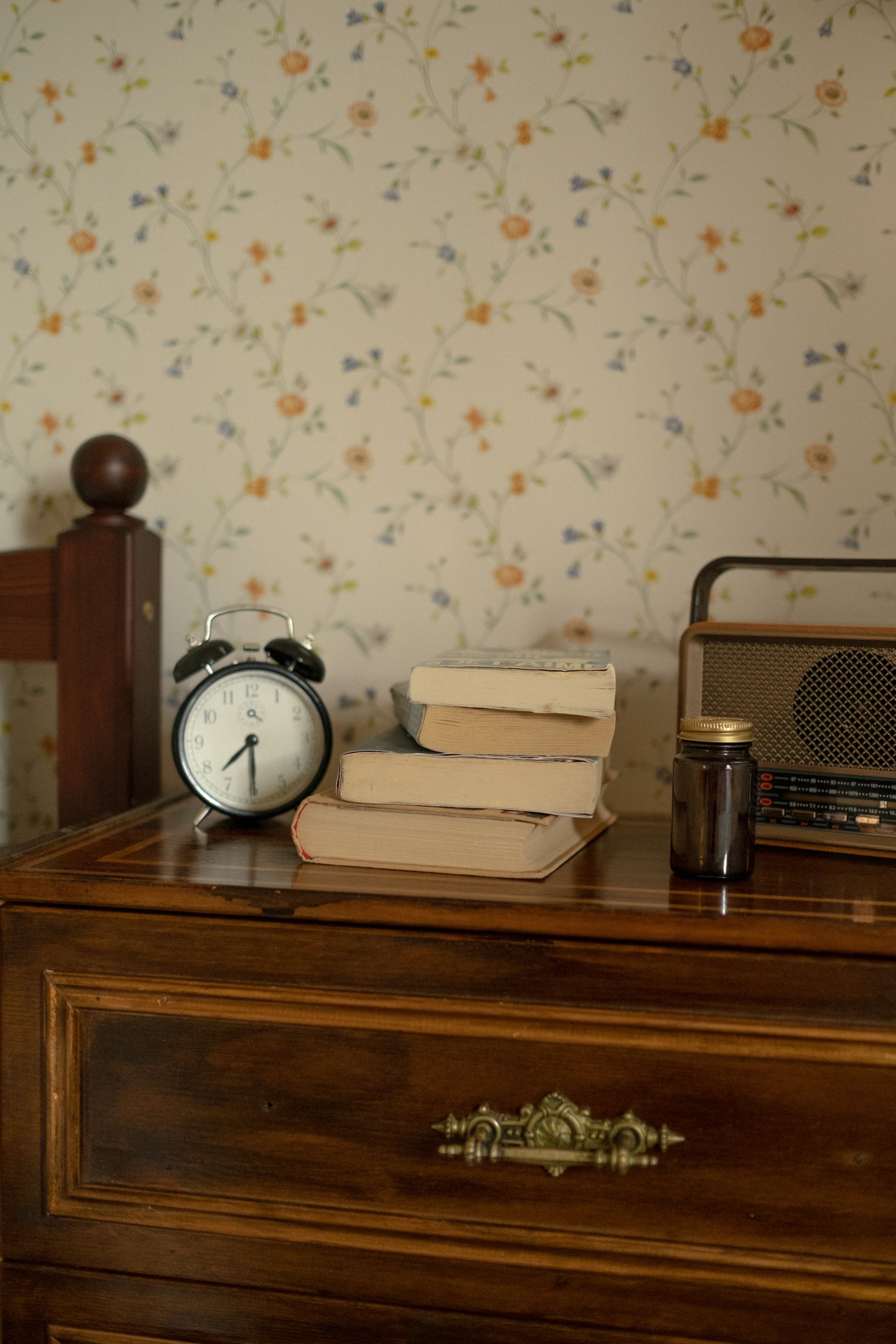 Retro alarm clock and radio resting on a warm wood chest of drawers with books