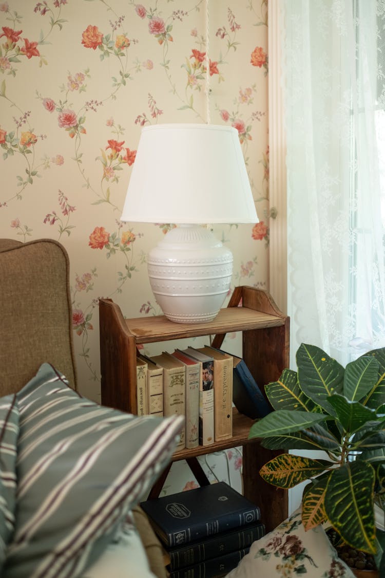 Lamp On Small Bookshelf In Room With Floral Wallpaper