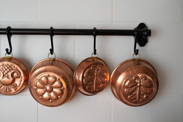 Old-Fashioned Copper Baking Pans Hanging On Wall In Kitchen