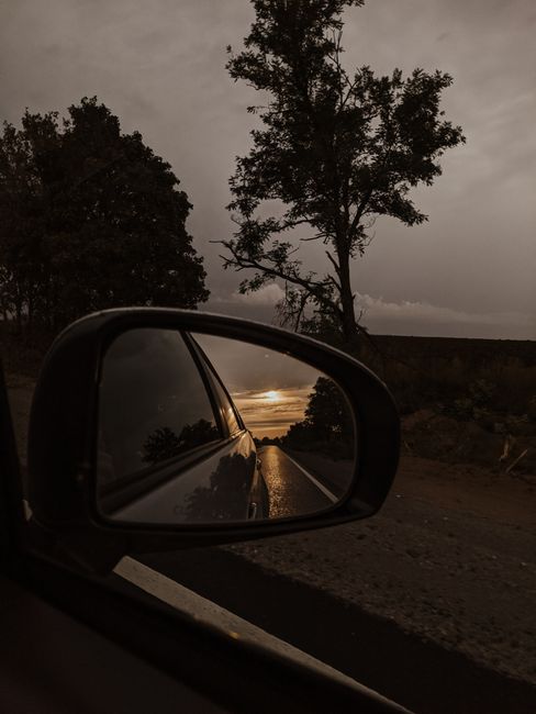A serene sunset reflected in a car mirror, surrounded by natural landscapes.