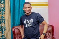 A cheerful man smiles warmly while posing indoors in Kinshasa, vibrant colors around.