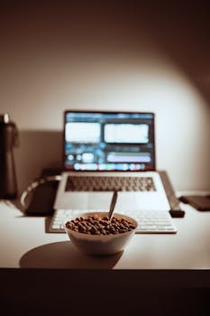 Bowl of cereal on a desk with a laptop, ideal for work-from-home setup imagery.