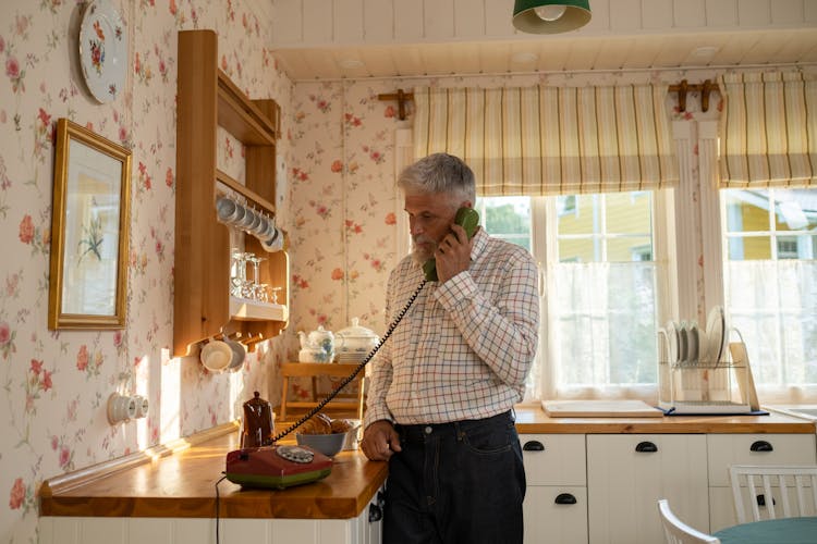 Senior Man Talking On Landline Phone In Old-Fashioned Kitchen