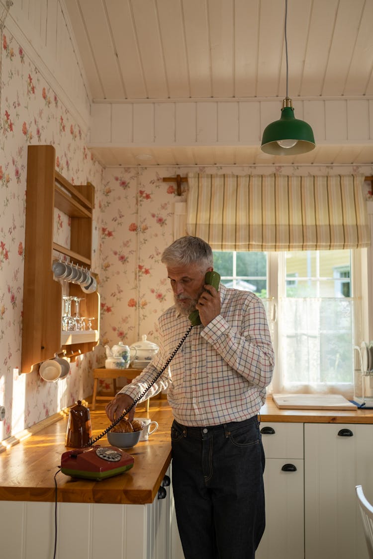 Senior Man Talking On Landline Phone In Old-Fashioned Kitchen