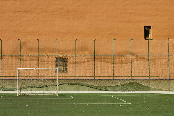 A lone soccer goal on an empty training pitch beside an ochre wall — photo by cottonbro studio on Pexels
