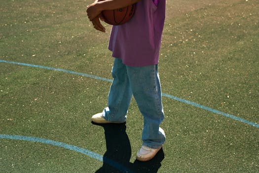 Person holding a basketball on an outdoor court in casual attire.