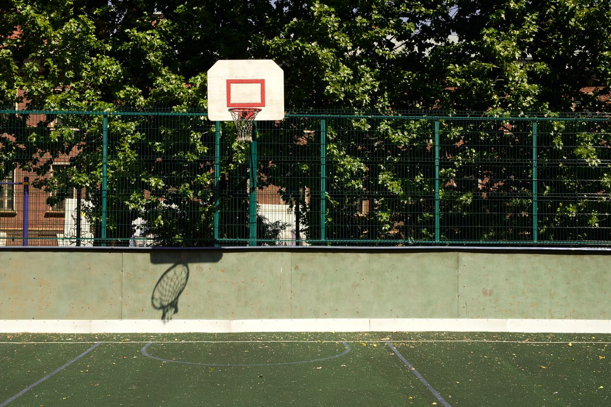 Sunlit outdoor basketball court and hoop behind a green fence — photo by cottonbro studio on Pexels