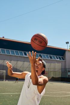 A young man with a mustache throwing a basketball on an outdoor sports ground during summer.