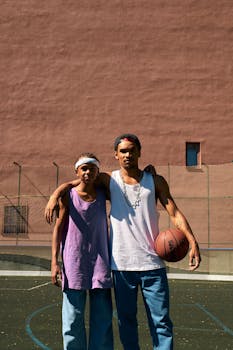 Two brothers in urban attire posing at a basketball court outdoors. Daytime shot.